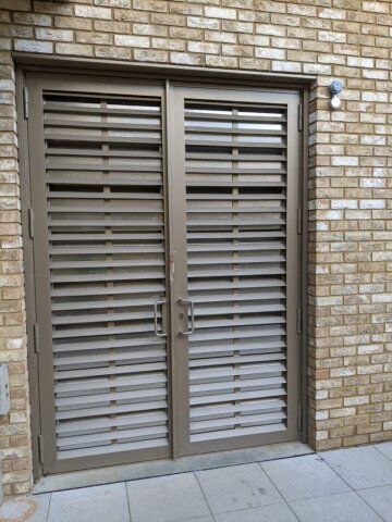 Acoustic Louvre Double Door achieving LPS1175 SR2 and SR3 standard designed and fabricated by Premier Security & Fire Ltd Louvre security doors with horizontal slats, designed for enhanced ventilation and security, set against a brick wall.
