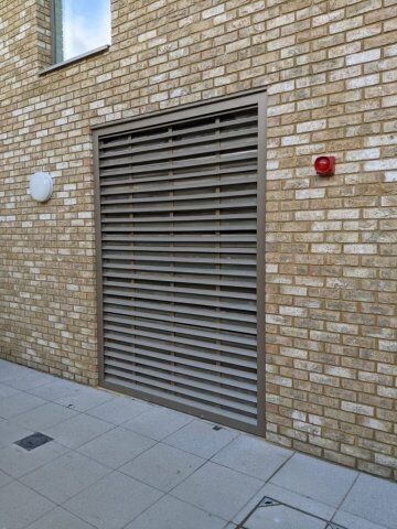 Acoustic steel louvre screen to LPS1175 SR3 & SR2 security standard made by Premier Security & Fire Consultants Ltd. Louvre security door installed in a brick wall, showcasing a modern design for enhanced safety and ventilation in commercial properties.