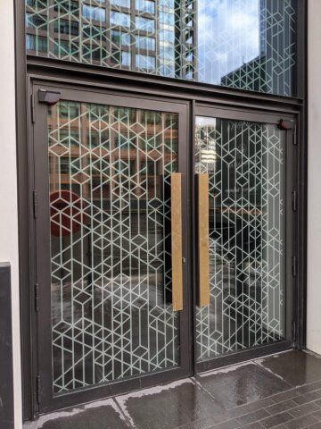 LPS1175 SR3 steel and glass communal entrance door Secure by Design accredited double doors with geometric patterned glass and wooden handles, showcasing modern security features for residential and commercial properties.