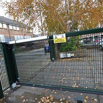 STEEL MESH GATES INSTALLED IN ESSEX Security gate with warning sign, surrounding trees and parking area, showcasing Secure by Design accredited access solutions for enhanced safety in residential and commercial properties.
