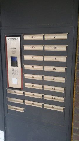Mailbox unit with numbered slots from 46 to 64, featuring an intercom system labeled "WORKPLACE" and a keypad, illustrating secure access for residents in a communal living setting.