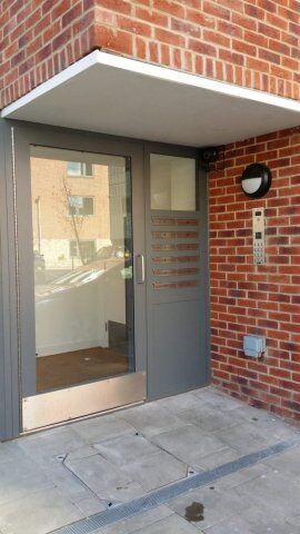 Secure by Design accredited entrance door with glass panel and intercom system, framed by brick wall, showcasing modern security solutions for residential or commercial properties.