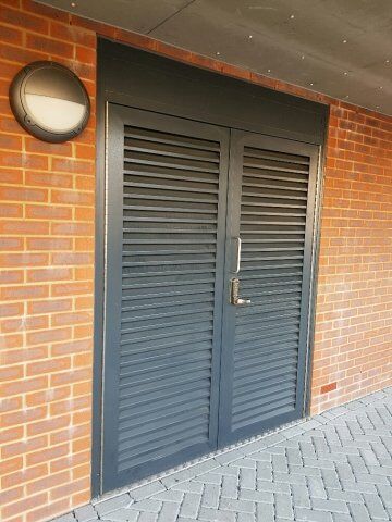 Secure by Design accredited louvre security door with robust locking mechanism, set against a brick wall, emphasizing strength and modern design for enhanced safety in residential and commercial properties.