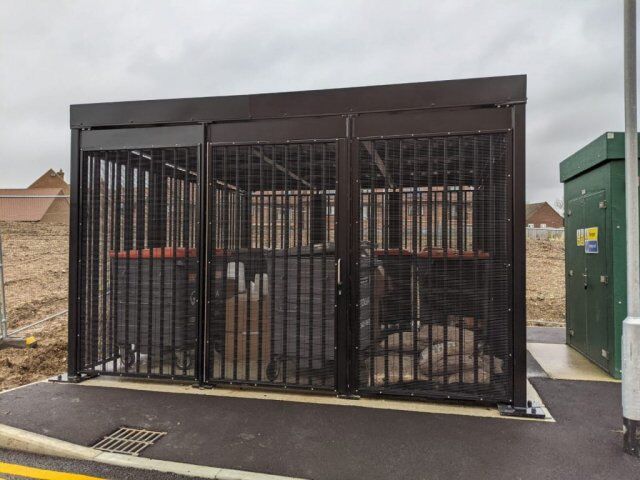 Bin store enclosure designed for security, featuring robust mesh fencing and a solid roof, certified to LPS1175 SR2 standards, situated in an outdoor setting.