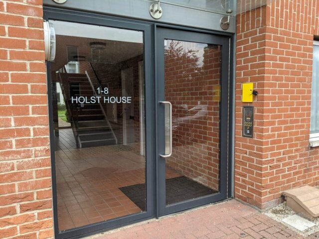 Secure by Design accredited communal entrance door with glass panels, featuring the address "1-8 HOLST HOUSE" and an intercom system, designed for enhanced security in residential buildings.