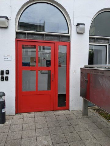 Secure red communal door with glass panels, showcasing modern design and security features, adjacent to a mailbox and access control system, reflecting Secure by Design principles.