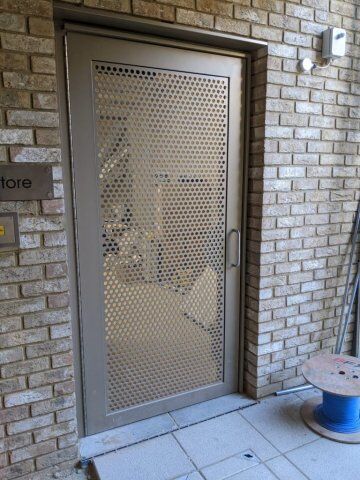 Industrial steel door with perforated design, enhancing security and ventilation, set against a brick wall, part of Secure by Design accredited range.