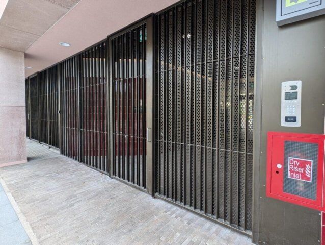Security gate with perforated metal design, integrated intercom system, and fire safety equipment, showcasing Secure by Design accredited features for enhanced safety in commercial properties.
