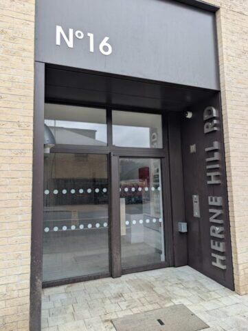 Entrance to a modern building at No. 16 Herne Hill Rd, featuring glass doors and a minimalist design, relevant to security installations and architectural aesthetics.