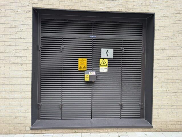 Security shuttered door with warning signs indicating electrical hazards, showcasing safety features relevant to Secure by Design accredited installations.