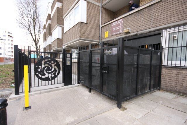 Secure by Design accredited gated entry with decorative metalwork, access control panel, and enclosed bin storage area in a residential setting.