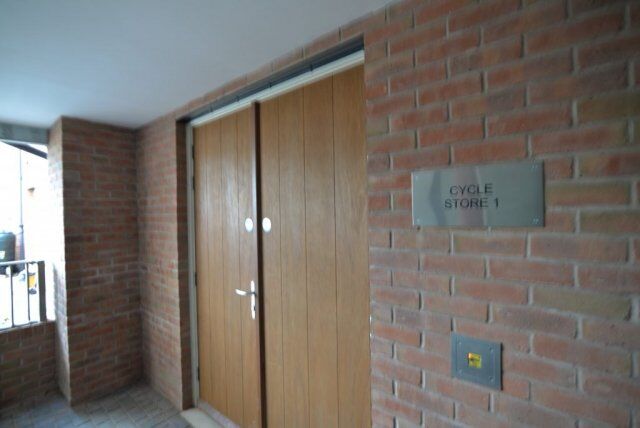 Wooden doors labeled "Cycle Store 1" in a brick corridor, highlighting secure access for bicycle storage in residential or commercial settings.