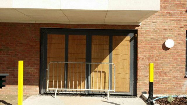 Industrial security door with wooden panels and metal frame, surrounded by a temporary barrier, in a brick building setting, highlighting Secure by Design accreditation.