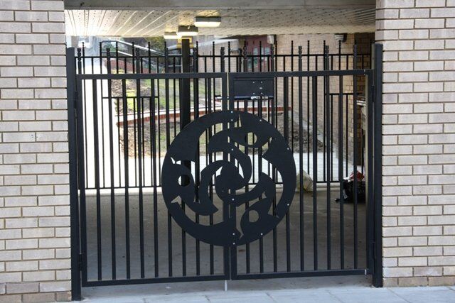 Black security gate with decorative circular design, providing access to a communal area, emphasizing aesthetic and functional security in residential settings.