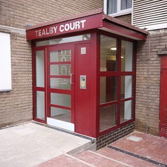 Secure by Design accredited entrance for Tealby Court, featuring a red framed door with glass panels, intercom system, and robust design, exemplifying high security standards for residential buildings.