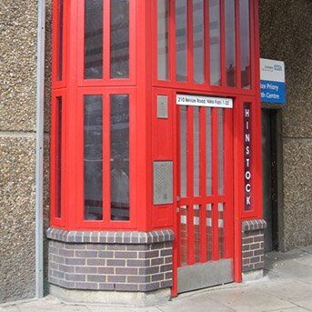 Red security door with glass panels and signage, showcasing a Secure by Design accredited installation for enhanced safety in communal areas.