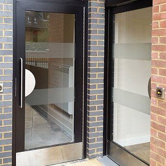 Secure by Design accredited communal doors with glass panels and stainless steel detailing, showcasing modern security features in a residential setting.