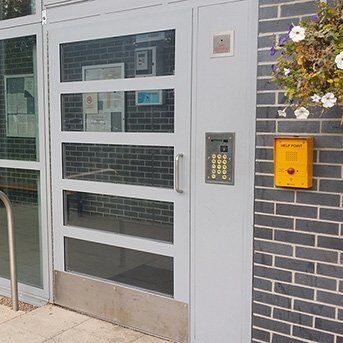 Secure by Design accredited entrance door with glass panels, keypad access control, and emergency call point, enhancing safety and security for residential and commercial properties.