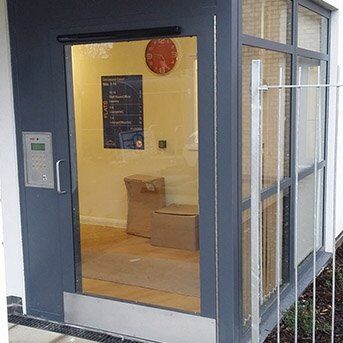 Secure by Design accredited communal entrance with glass panels, electronic access system, and visible interior seating area.