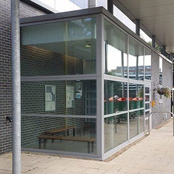 Modern glass and steel security entrance with bench, showcasing Secure by Design principles in architectural design.