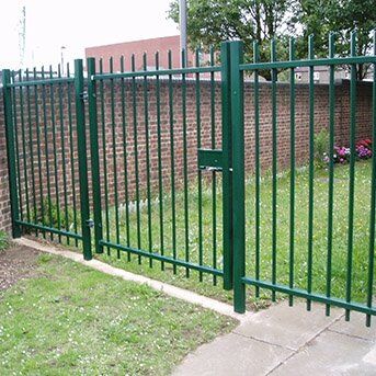 Green security gate with vertical bars, providing access control for residential or commercial properties, surrounded by grass and brick wall, emphasizing high-standard security solutions.