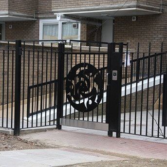 Black security gate with decorative circular design, leading to a communal area in a residential setting, showcasing Secure by Design accreditation.