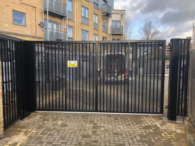 Secure by Design accredited security gate with vertical bars, providing access control to a communal area, surrounded by residential buildings.