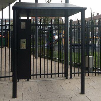 Secure by Design accredited security gate with intercom system, surrounded by a vertical metal fence and green landscaping, emphasizing safety and access control.