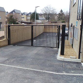 Secure by Design accredited security gate with black metal frame, leading to a paved parking area, showcasing enhanced safety for residential and commercial properties.