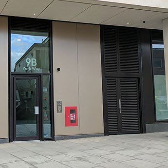 Modern building entrance featuring security door with louvre panels, address "9B York Way," and fire alarm box, emphasizing Secure by Design principles.