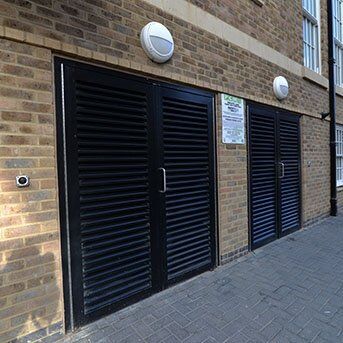 Louvre security doors in a brick wall setting, featuring black slatted design, enhancing safety and aesthetics for residential or commercial properties.