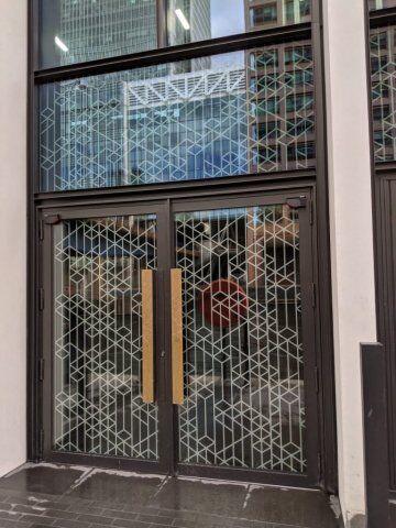 Secure by Design accredited glass doors with geometric patterns and wooden handles, showcasing modern security design for commercial properties.