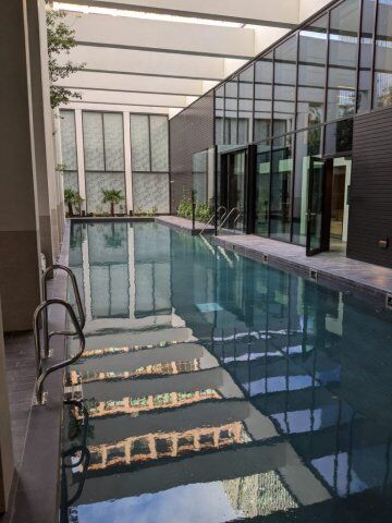Indoor swimming pool with glass enclosure, modern architecture, and reflections of surrounding buildings in the water.