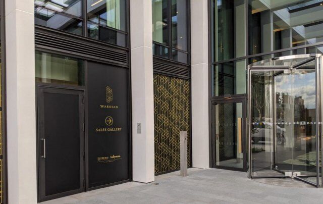 Entrance of the Wardian Sales Gallery featuring modern architecture, glass doors, and decorative wall design, emphasizing security and aesthetic appeal in a commercial setting.